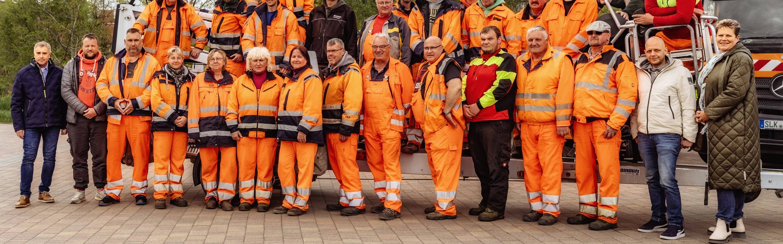 Alle Außendienstmitarbeiter des Stadtpflegebetriebes präsentieren sich in ihrer orangefarbenen Arbeitskleidung als Gruppe auf dem Gelände des Eigenbetriebes